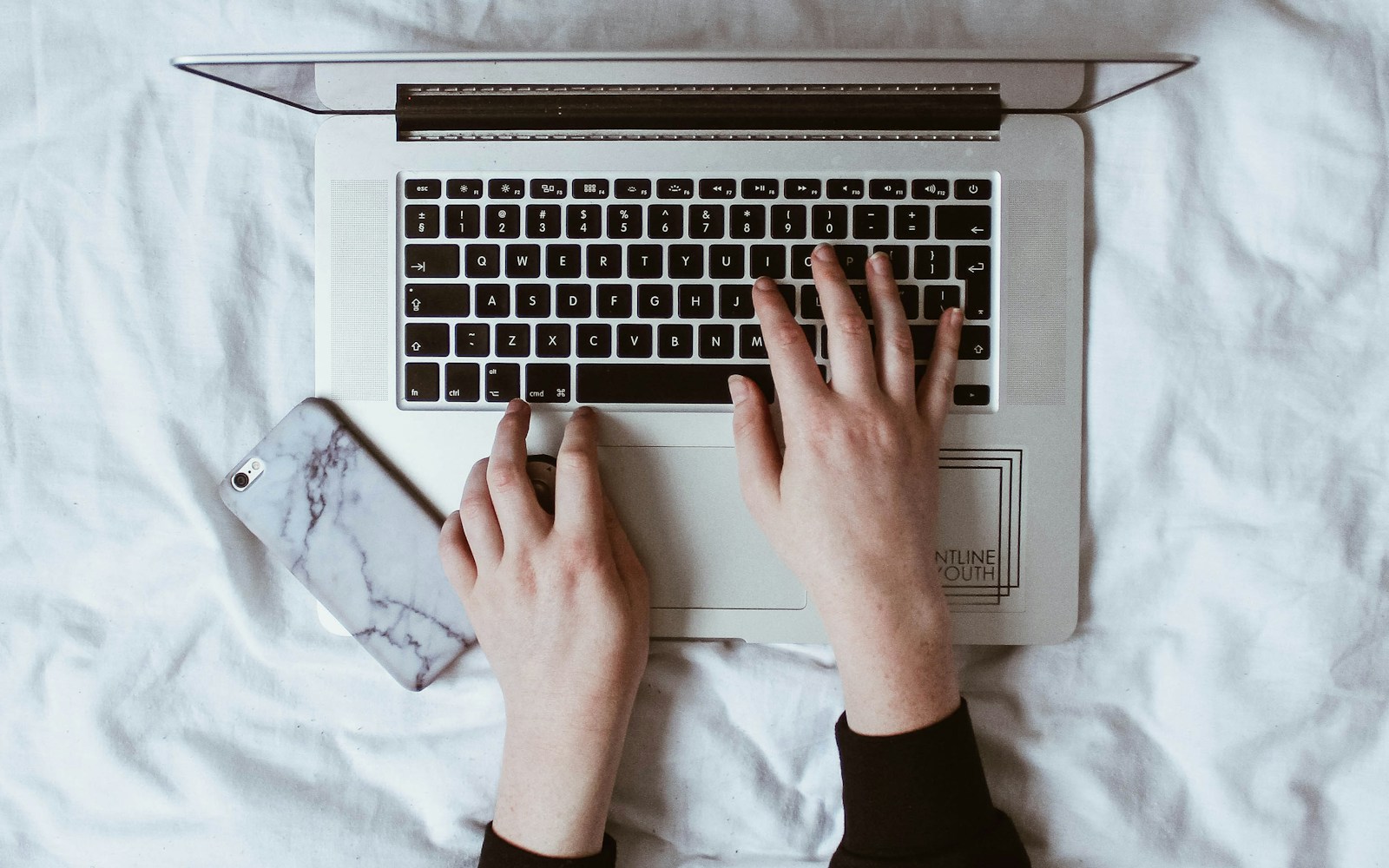 Hände an einem Laptop mit einem Smartphone daneben
